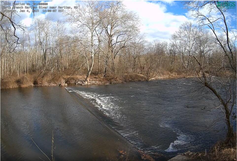 Looking down upon a weir creating a small drop and turbulence in a river with bare winter trees on the far bank