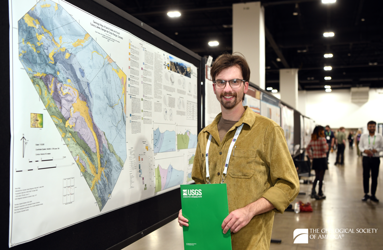 A person stands to the right side of a poster with a colorful geologic map and several cross sections.