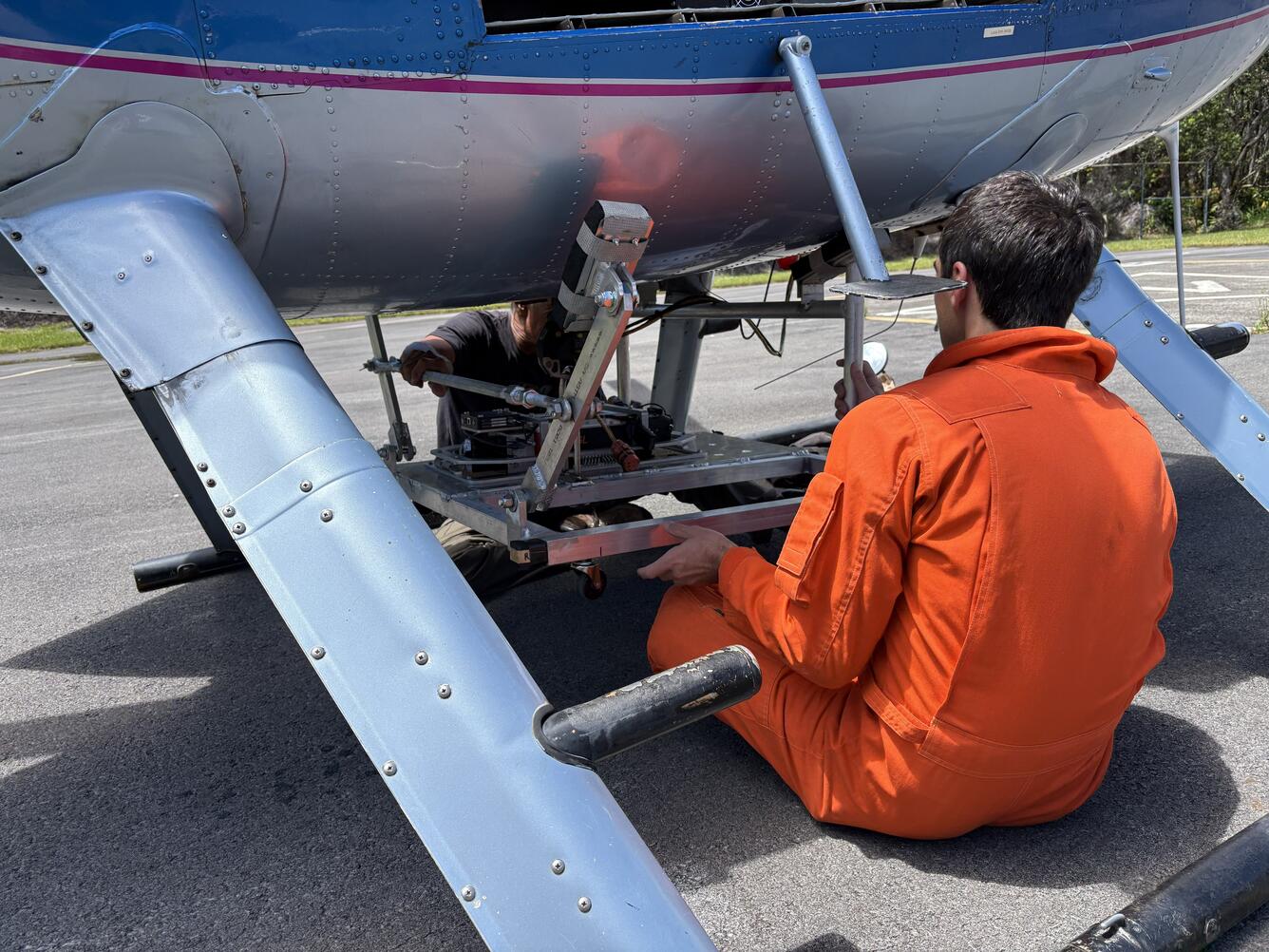 Color photograph of scientist mounting equipment at base of helicopter