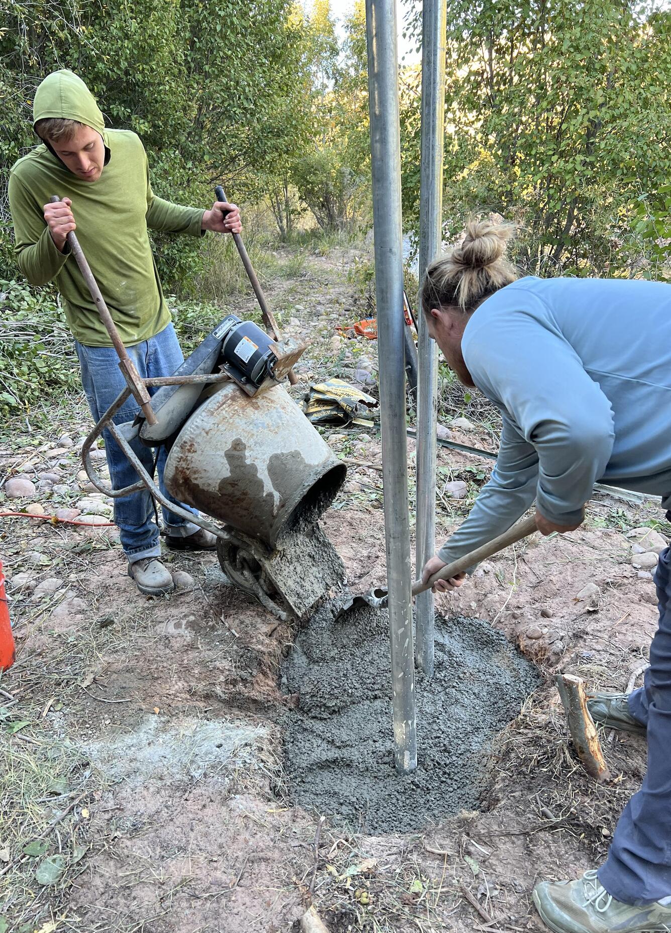 Two men pour concrete to secure upright posts.