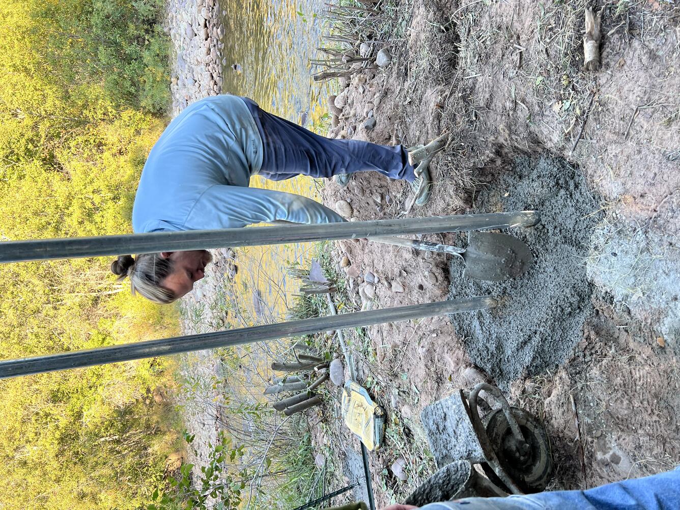 Man smooths newly poured concrete with a shovel to secure upright posts.