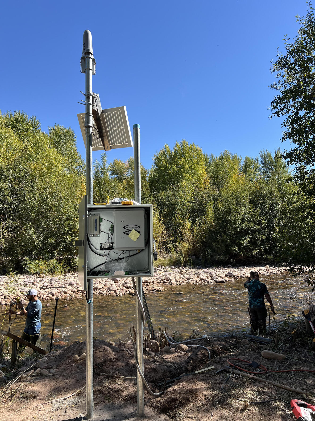 Finished stream gage showing instruments with two men and stream in background 