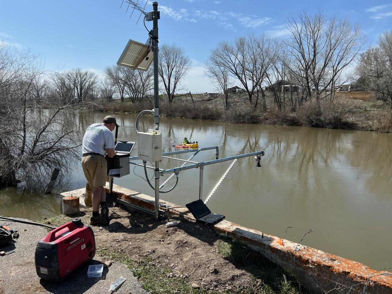 Man on river's edge checking instrumentation at gaging station.