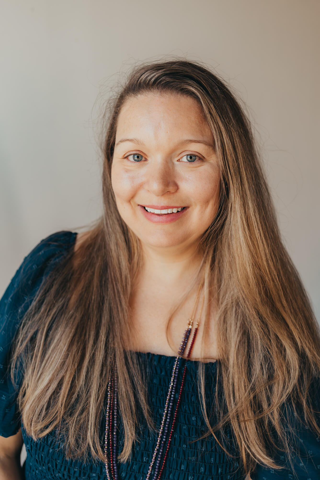 woman with blue eyes and long blonde hair wearing a green sweater and beaded necklace