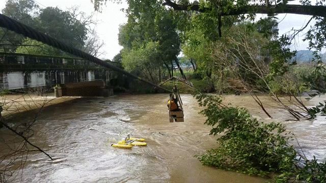 10-second video of rushing water in a stream. Person in a small car suspended from overhead cableway, instruments hanging below