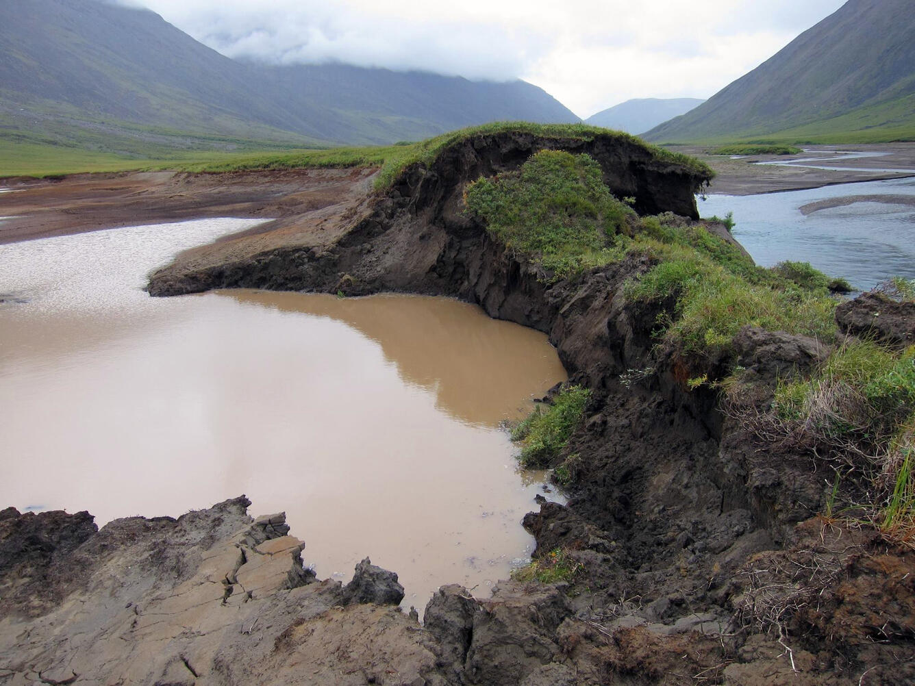 Muddy water next to a river with mountains in distance