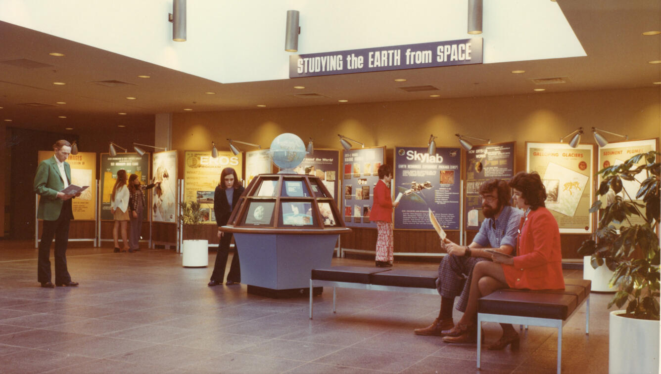 People are scattered around a lobby with a globe in the center in the 1970s