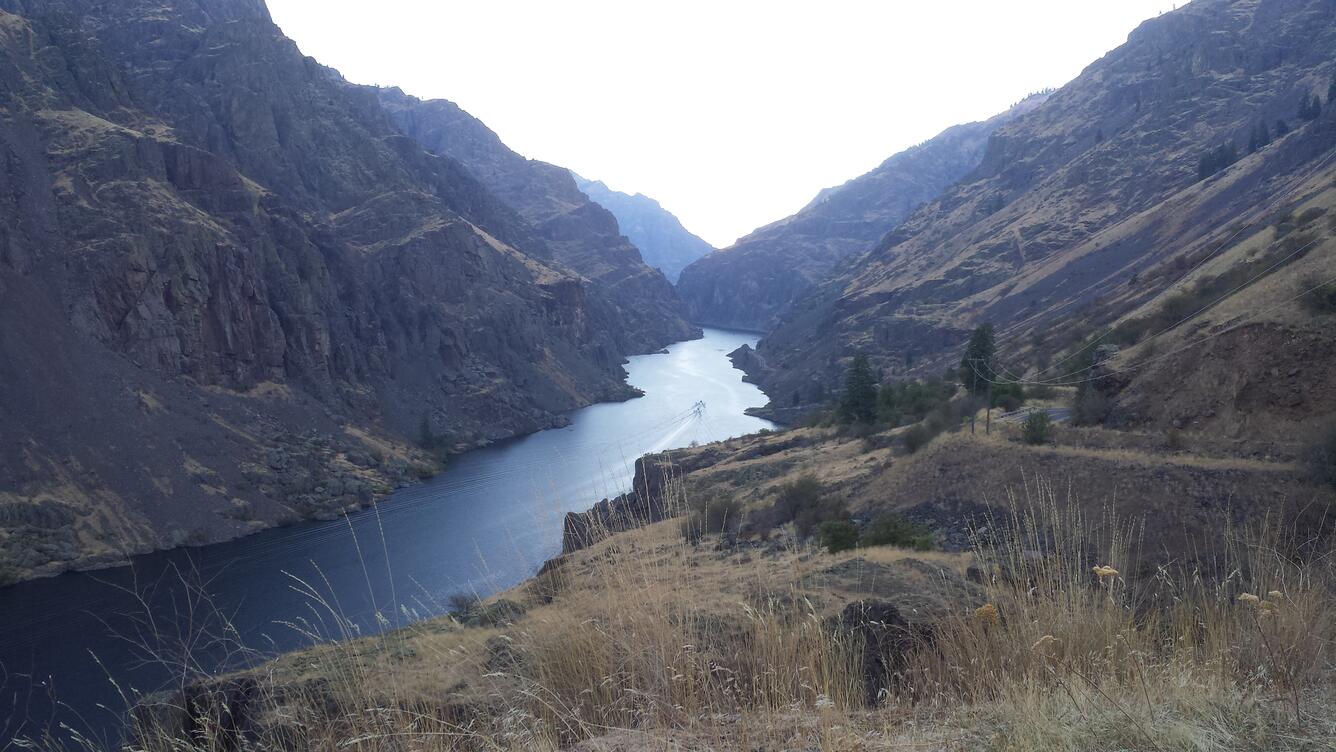 blue Snake River water running through an arid, high desert canyon. Two boats are travelling on the river into the distance.