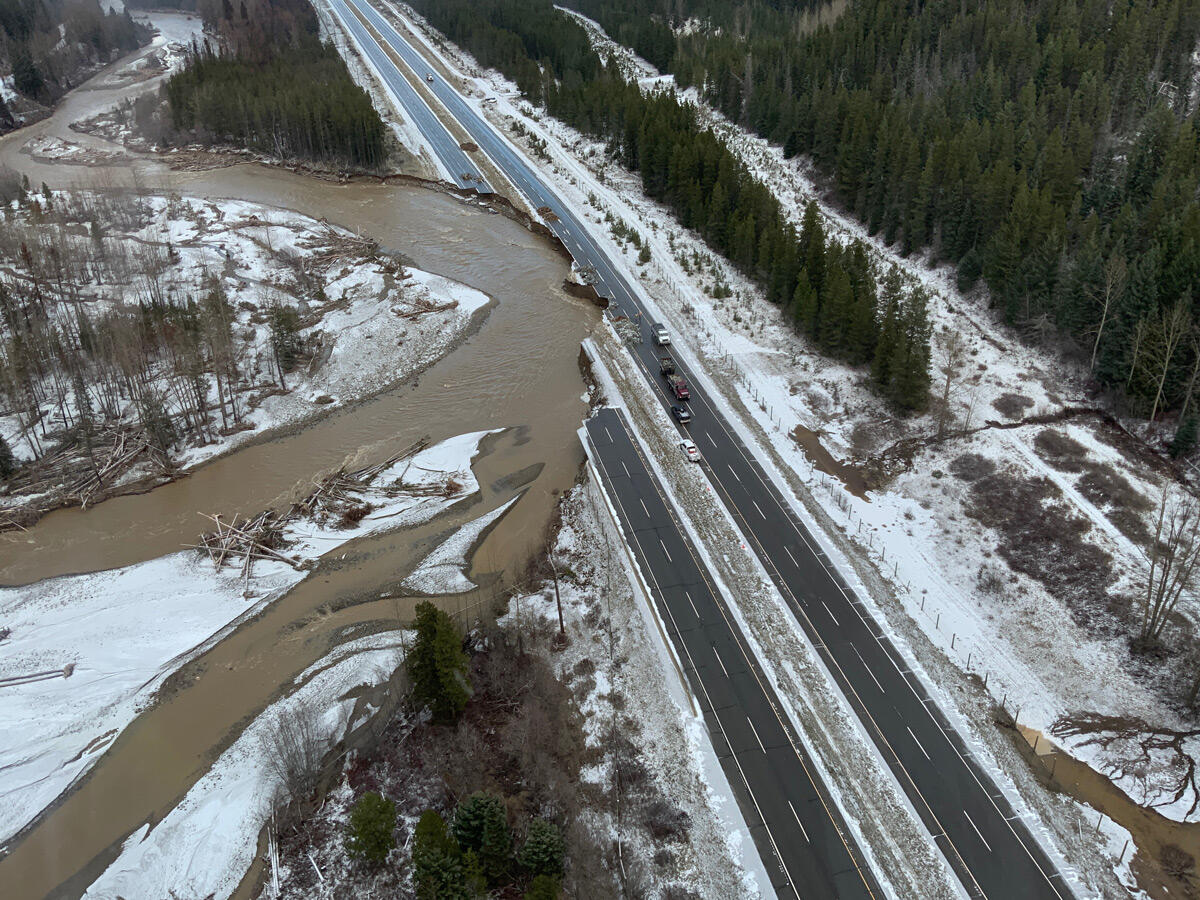 snowy 2-lane highway with river flowing next to it that has cut into both roads