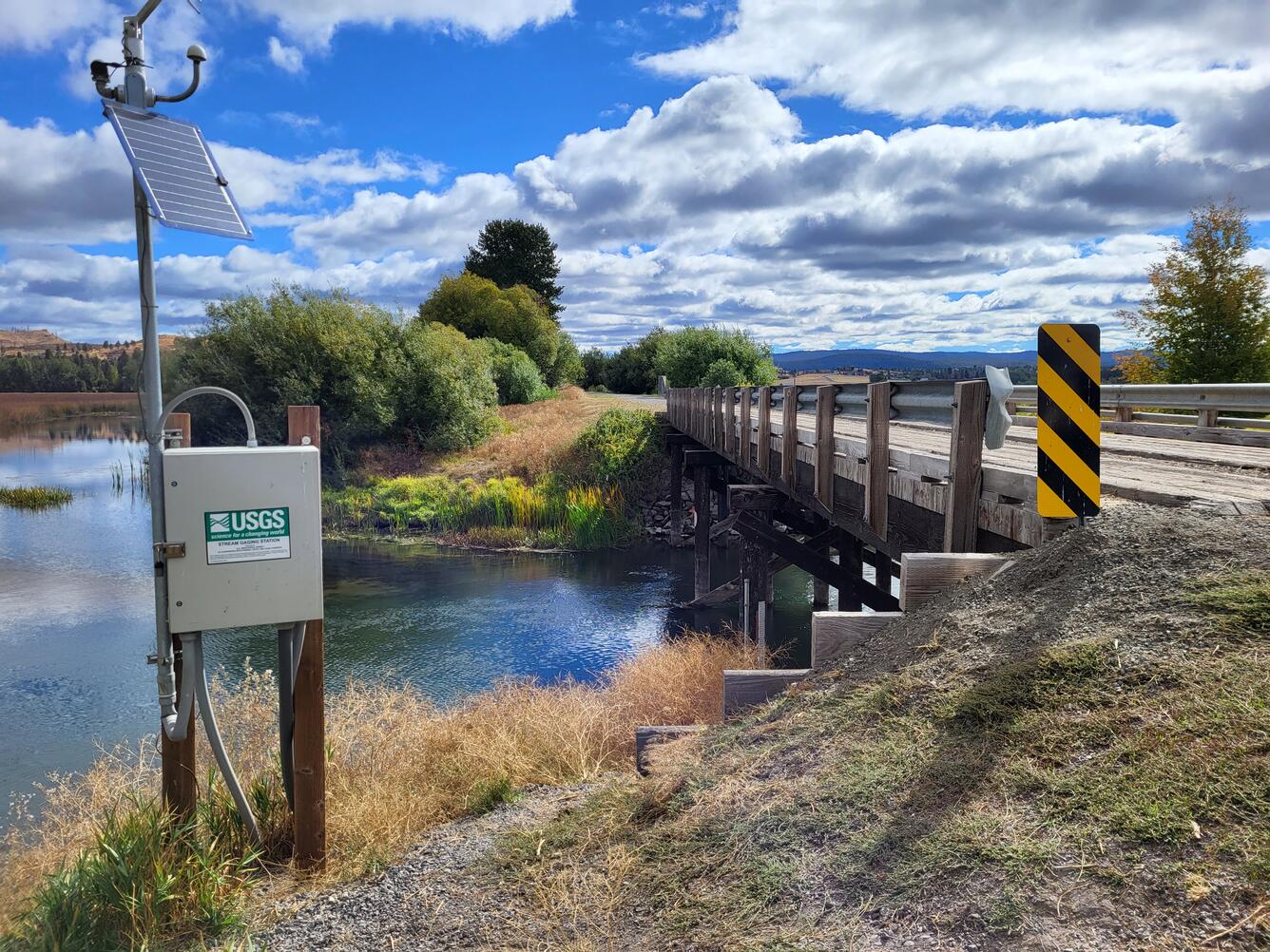 Pole mounted metal gage box next to a river flowing under bridge