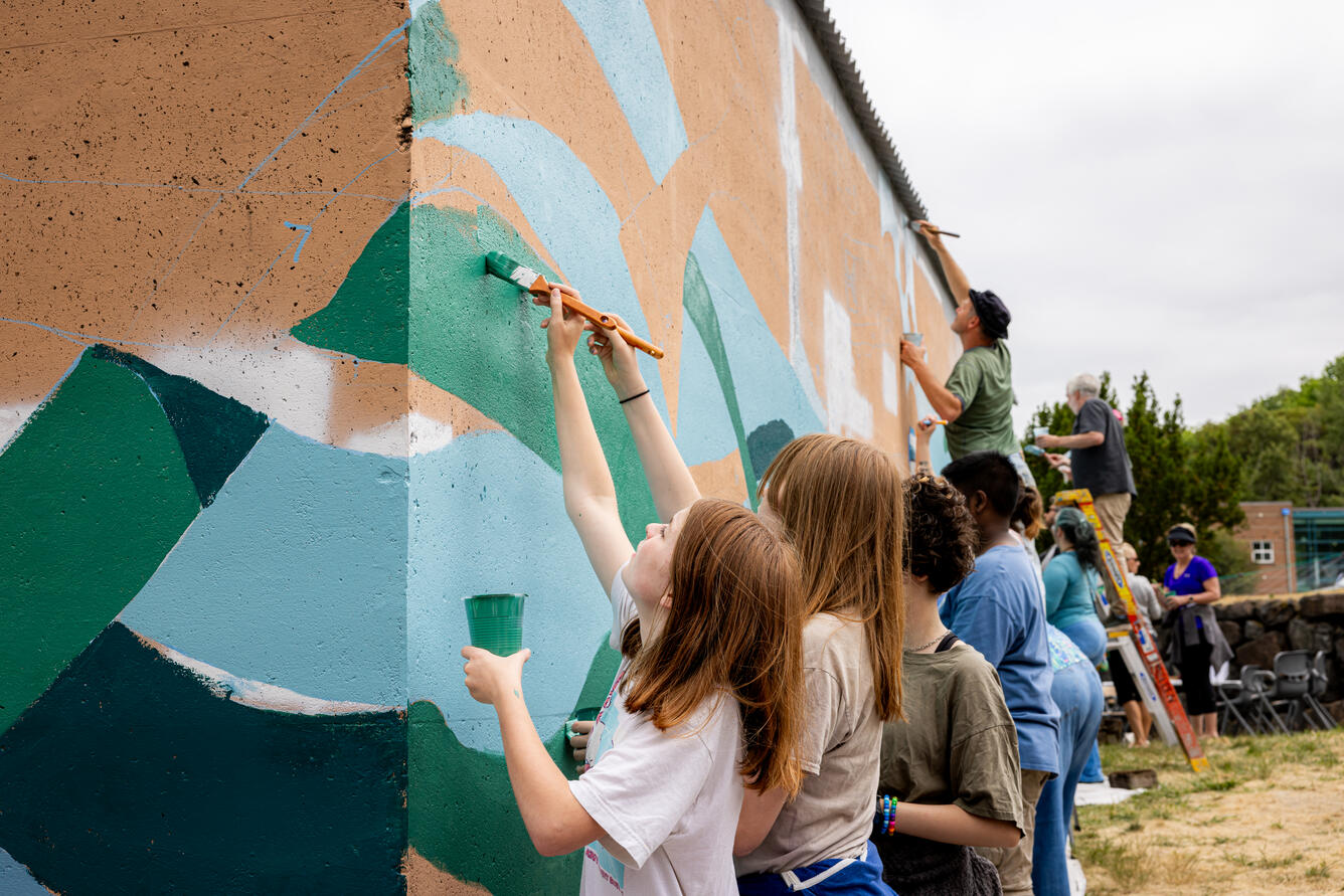 Volunteers of all ages painting a mural on the WFRC storage building