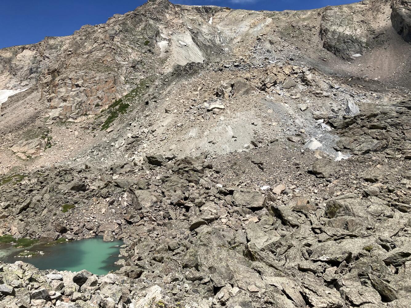 Blue lake surrounded by boulders with rocky hillslope in the background