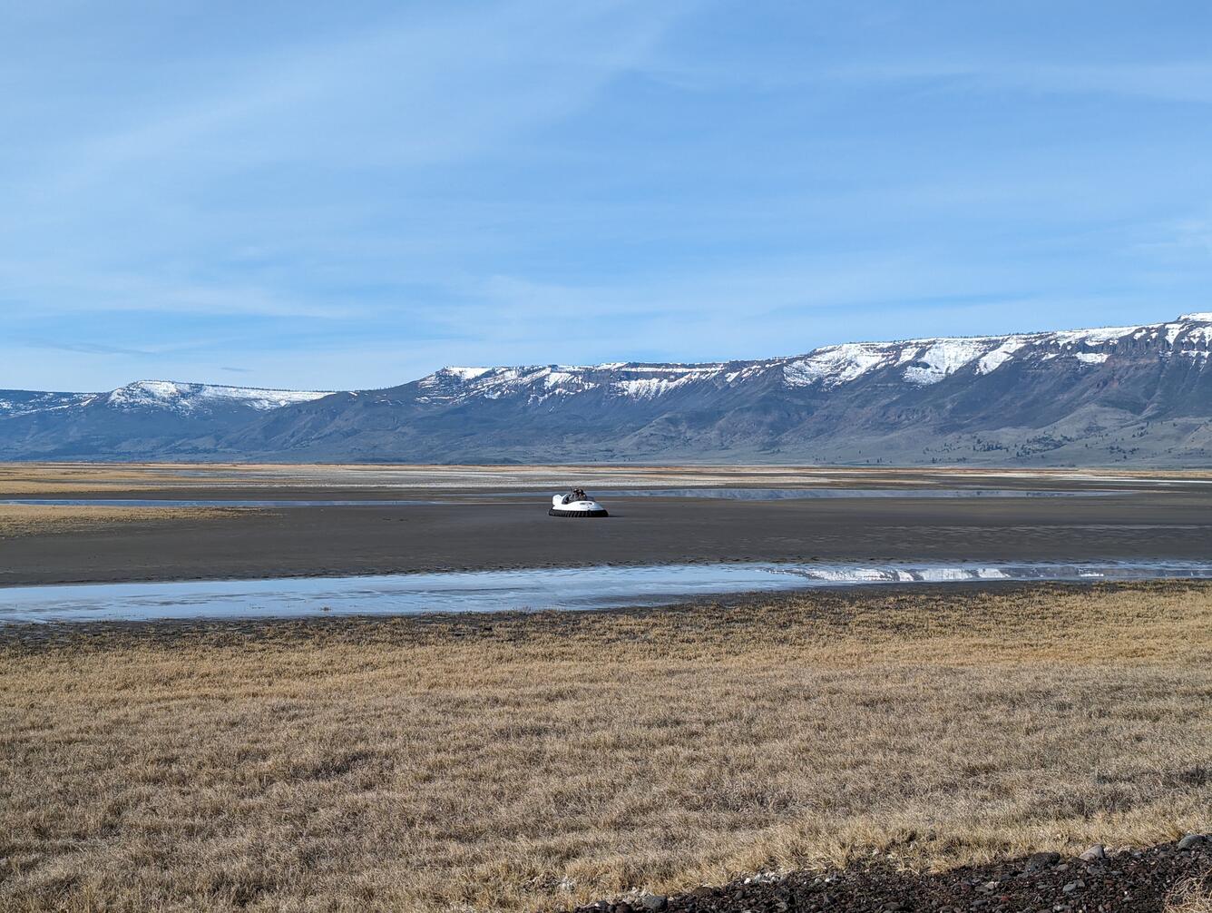a hovercraft sits atop a mudflat with mountains in the background
