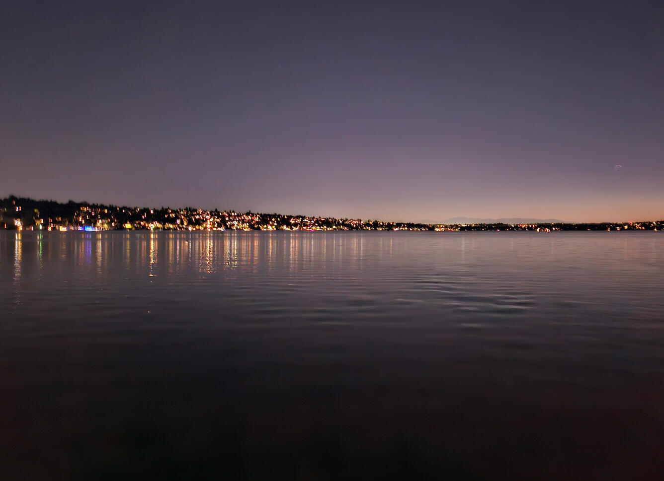 skyline at night with lots of artificial light from houses and buildings along the lake
