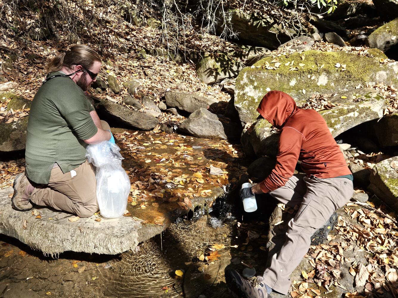 Two USGS scientists collect a water quality sample from a mountain creek