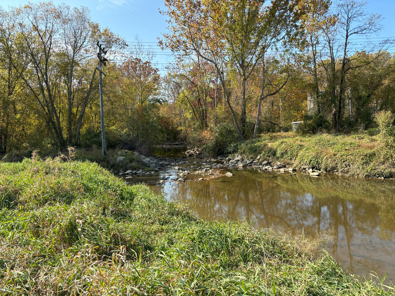 An urban creek in autumn with a bridge in the background.