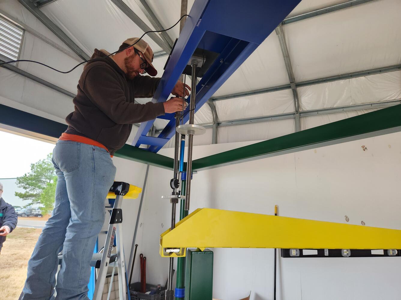 A USGS technician standing on a ladder works on the instrument table above the West Point Extensometer.