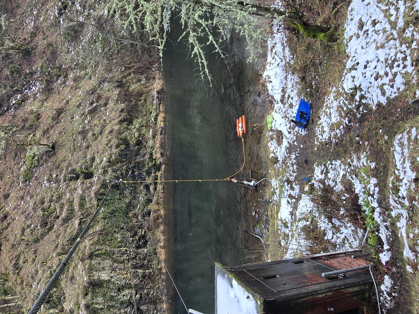 ADCP sensors in a small orange trimaran attached to cable with a rope. Narrow river with steep rocky banks.