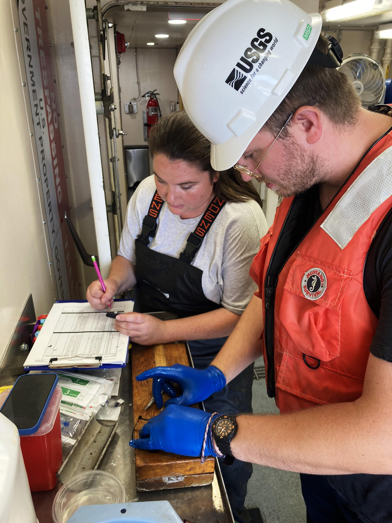 On a large research vessel, a researcher collecting a sample for glucose analysis and another recording the information
