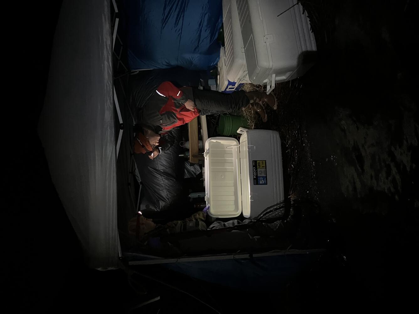 Photo of scientist in red and black jacket out in tent bent over cooler with fish in Klamath Falls, OR