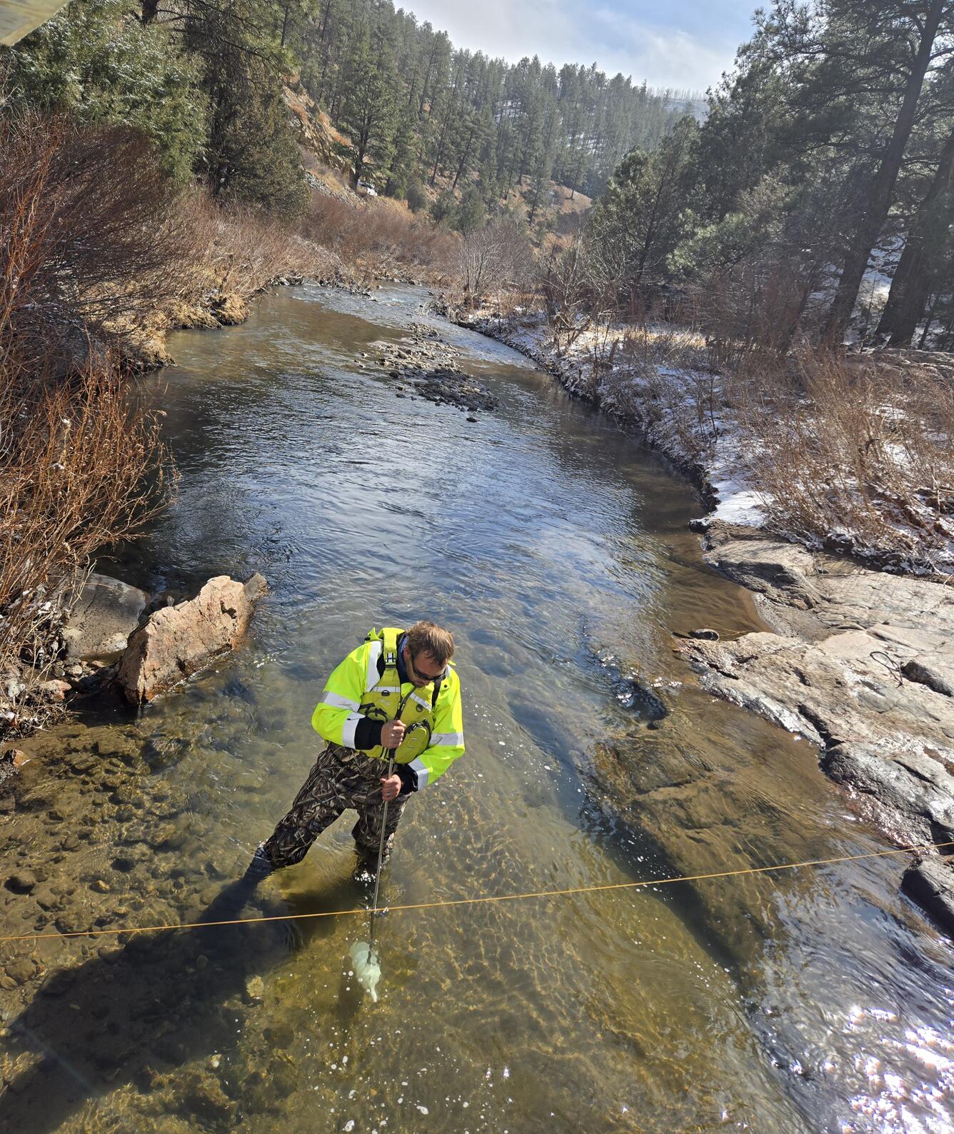 A hydrologist stands in a low-flowing creek and is holding a sampling bottle under water
