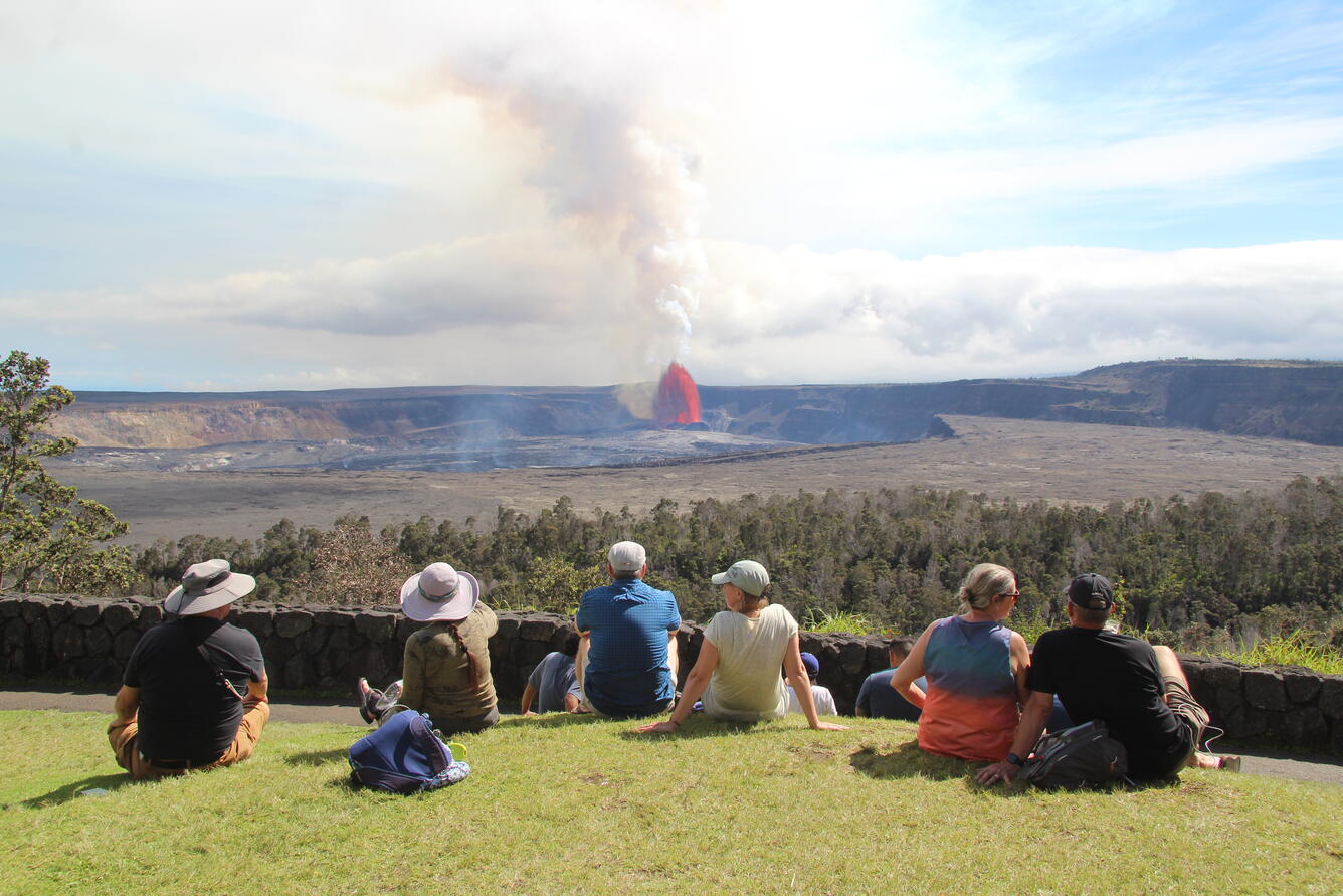 Color photograph of people sitting on grass watching volcanic eruption