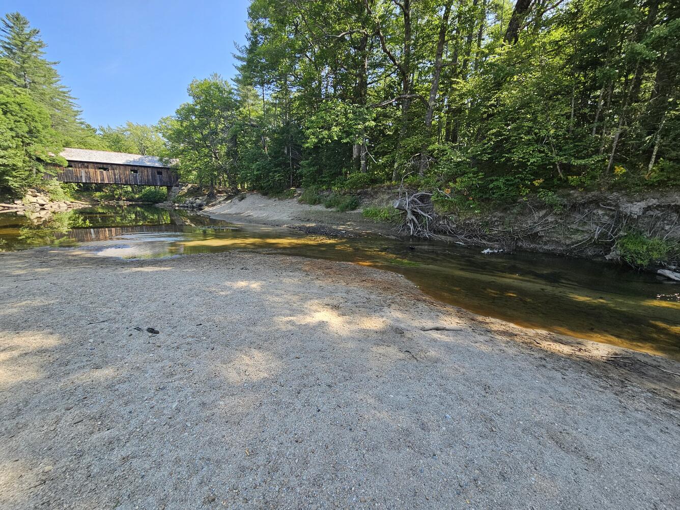 A dry riverbed with a covered bridge in the background.