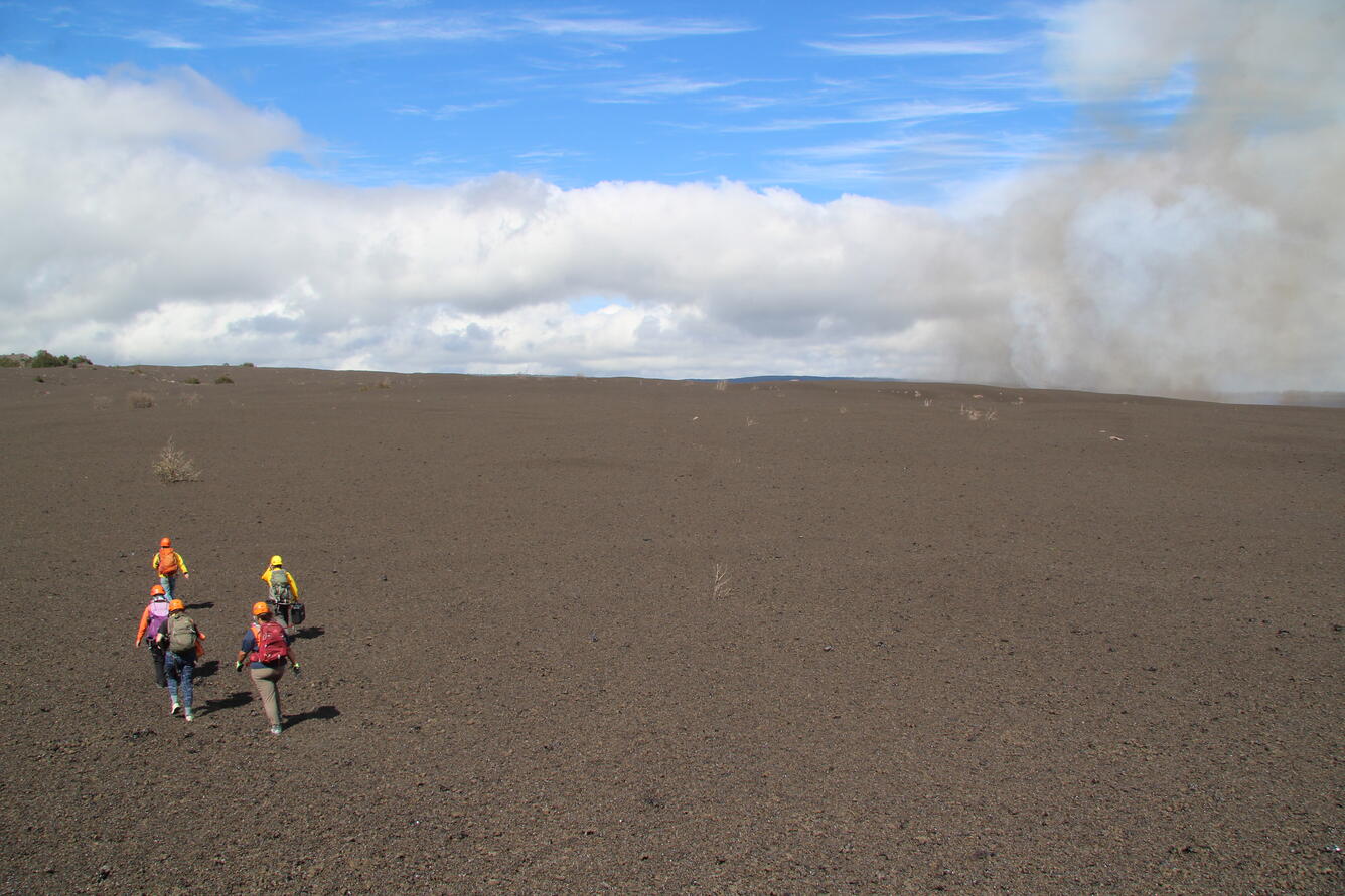 Color photograph of scientists walking across volcanic terrain to monitor eruption