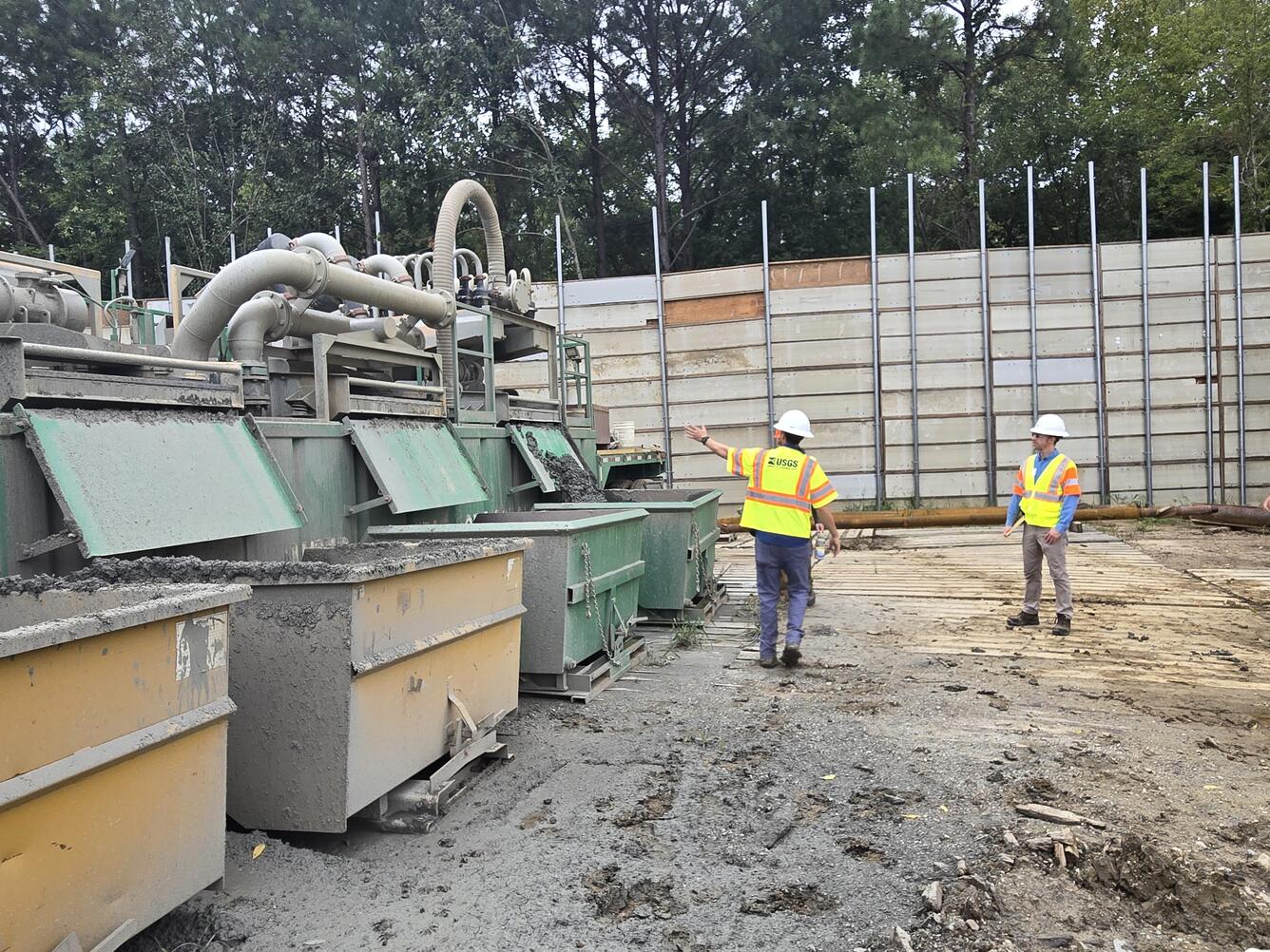 A USGS scientists leads a tour of a drilling site. He indicates where drilled sediments are deposited out of the shaker.