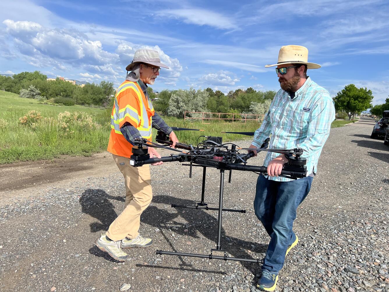 Two pilots carry drone aircraft on gravelly road