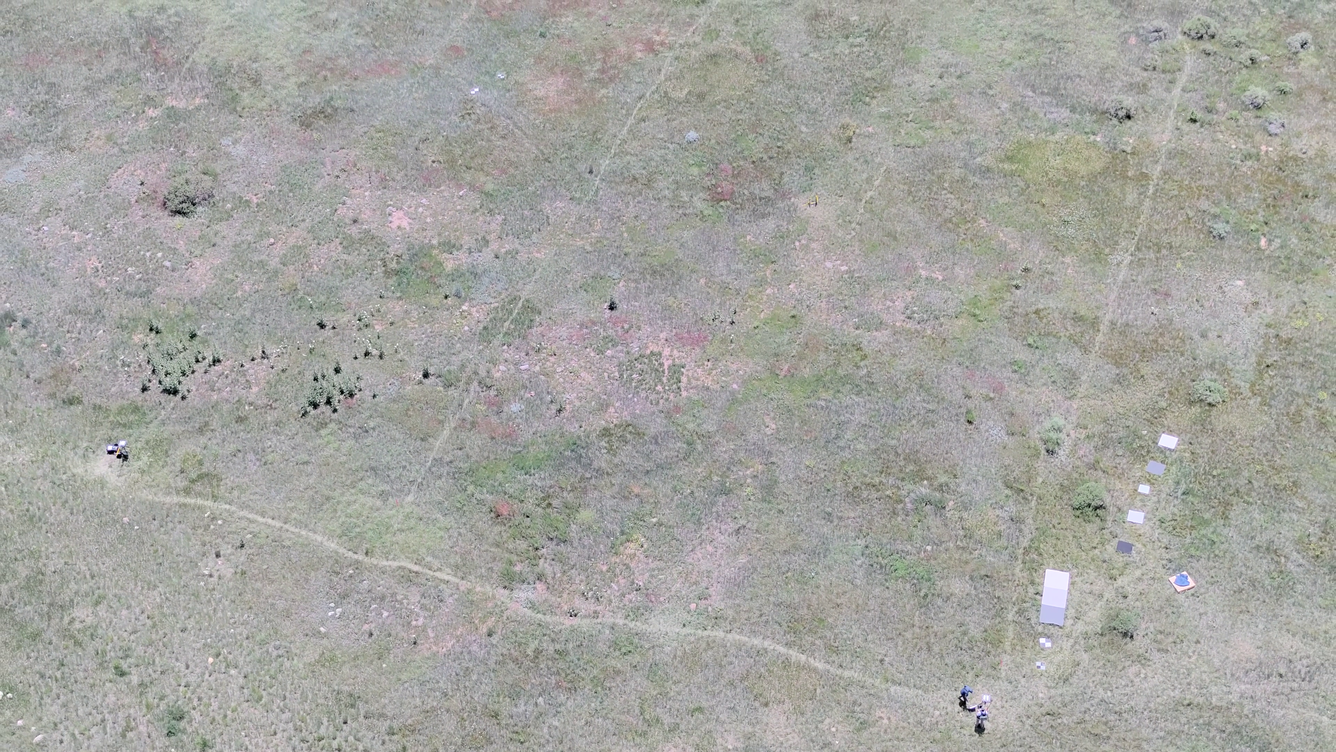 Aerial photo looking down at a field with drone operator and reference objects used for calibration of payload instruments