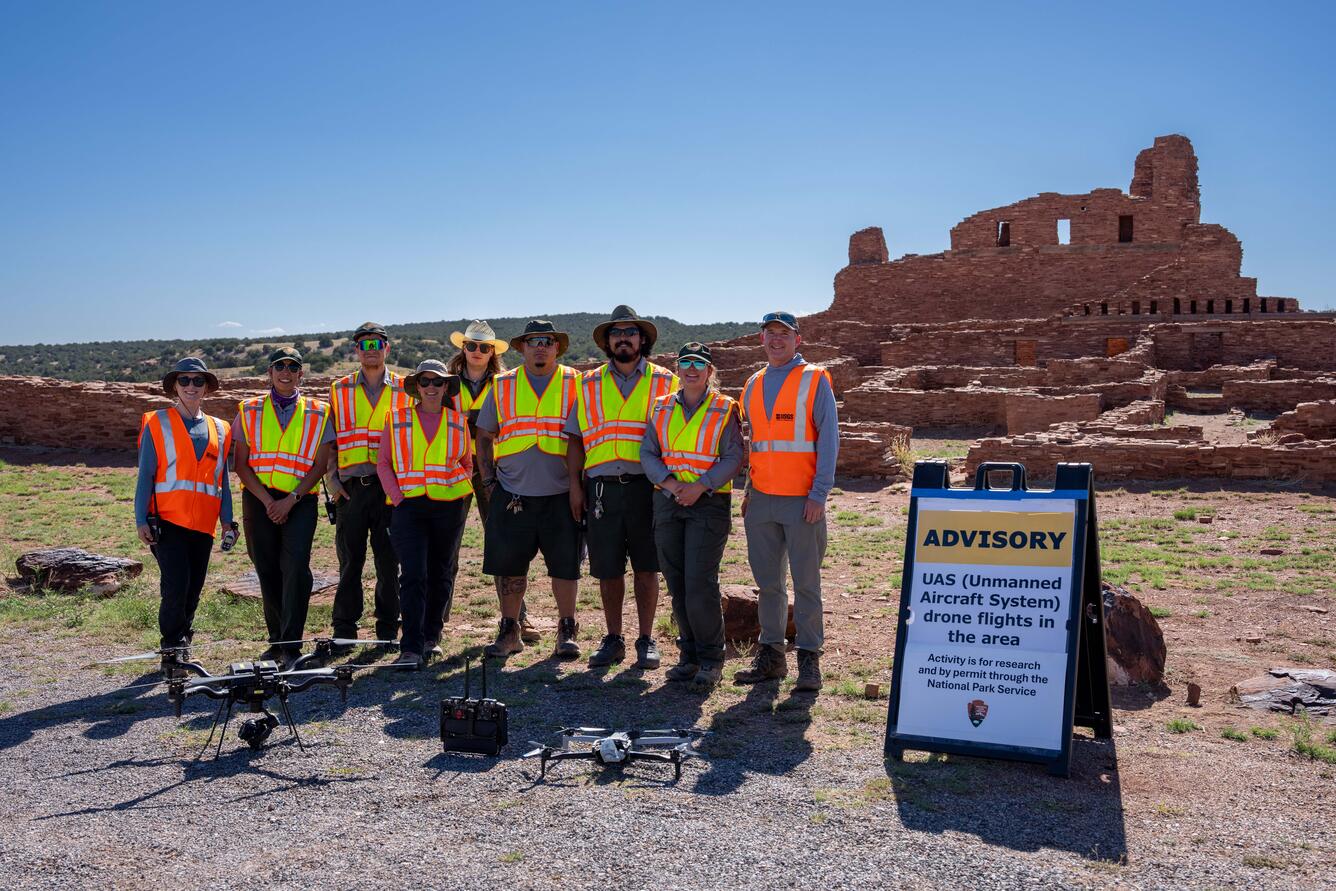 USGS and National Park workers pose with drone in front of stone structure at Abó Ruins