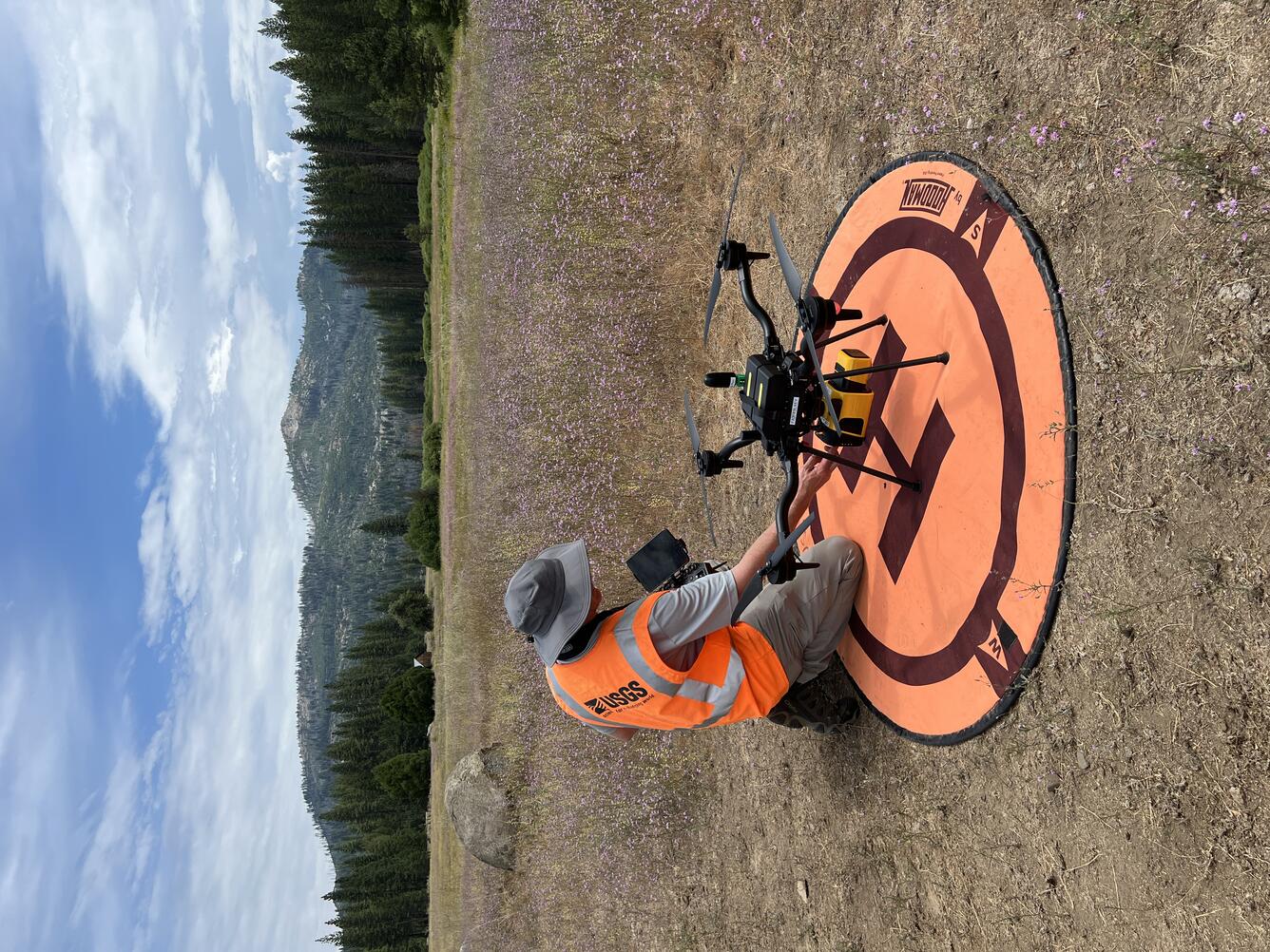 UAS pilot readying craft that sits on landing pad situated in a mountain clearing