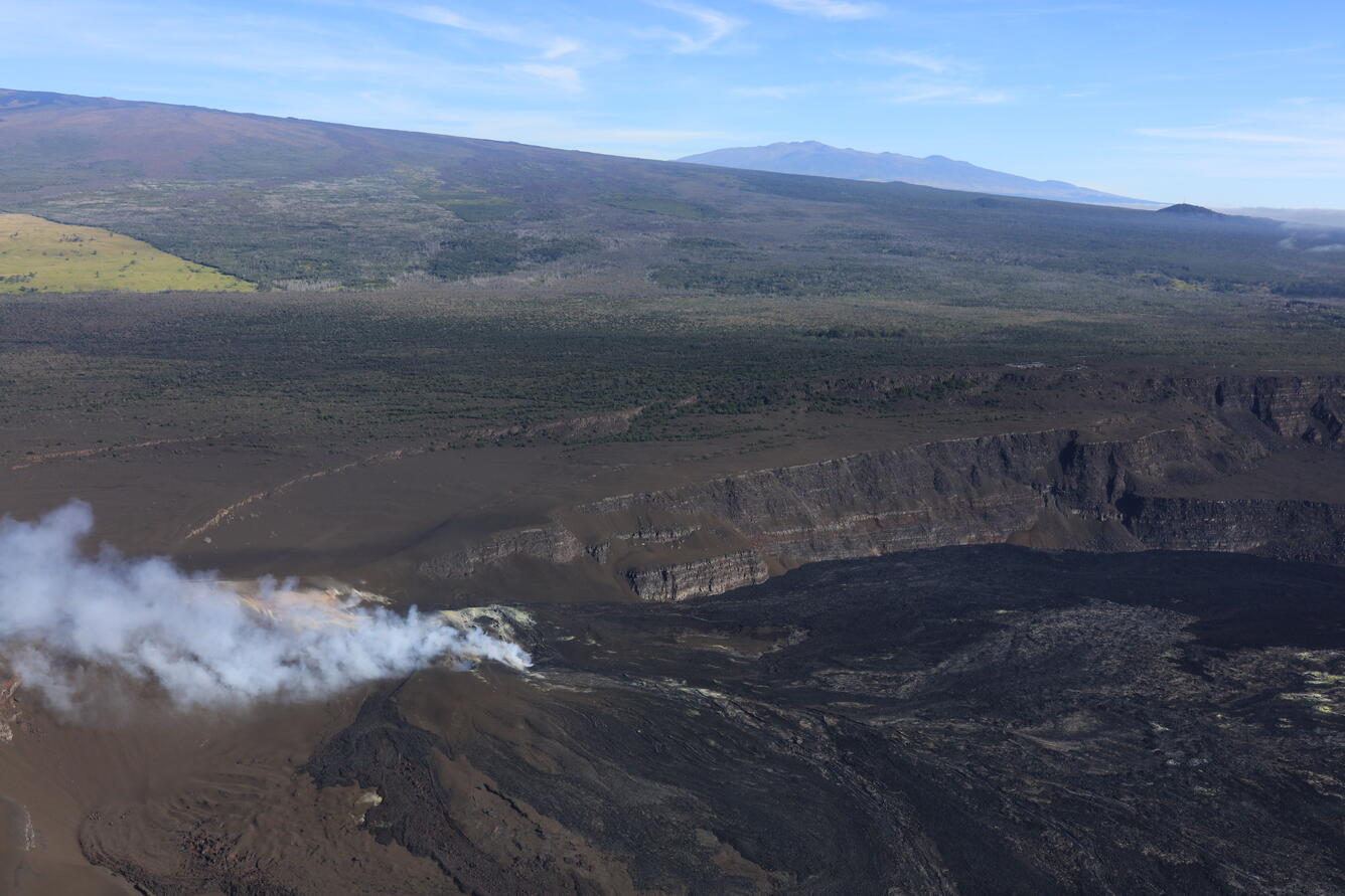 Color photograph of crater at summit of volcano with another volcano in background