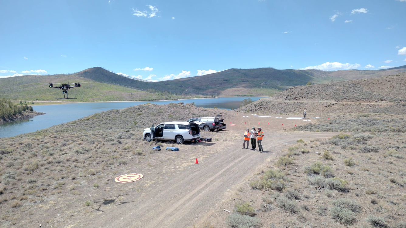 UAS personnel stand next to their vehicles as they control drone above reservoir