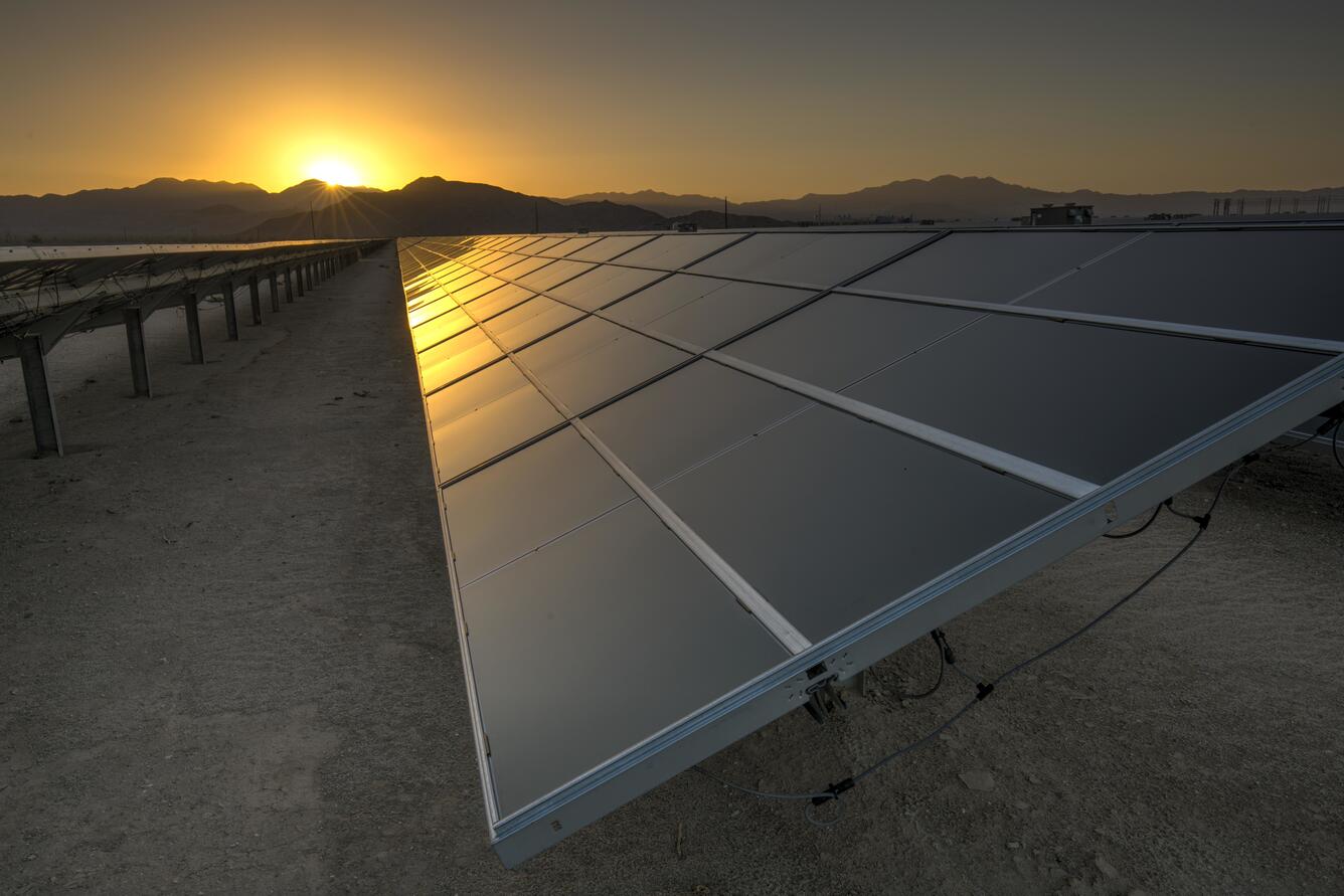 Solar panels in the California desert with the sun setting behind mountains in the distance
