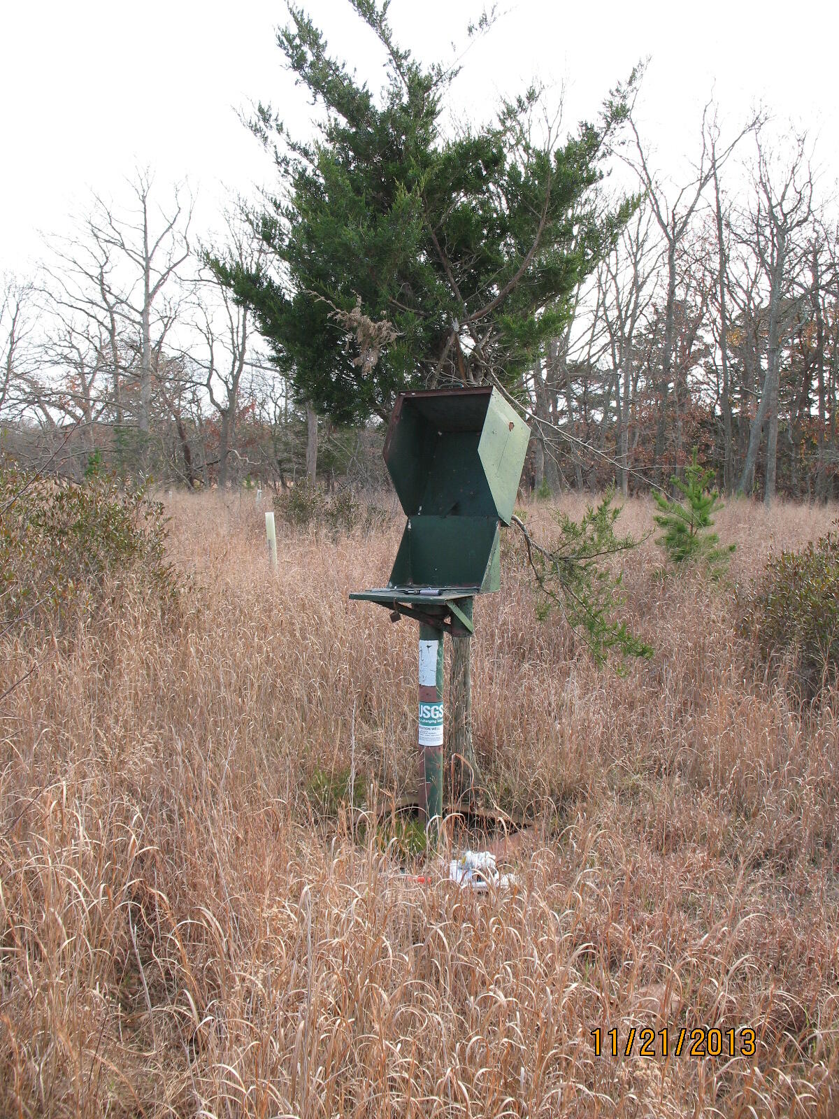 A well standpipe with an open access box on top stands in the middle of a grassy field