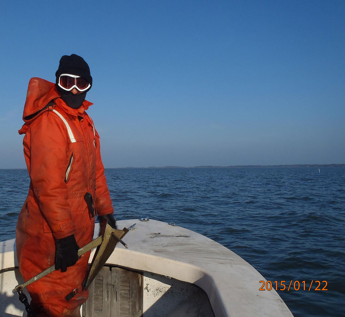 Image shows USGS scientist on a boat holding the anchor, preparing to drop it in the water.