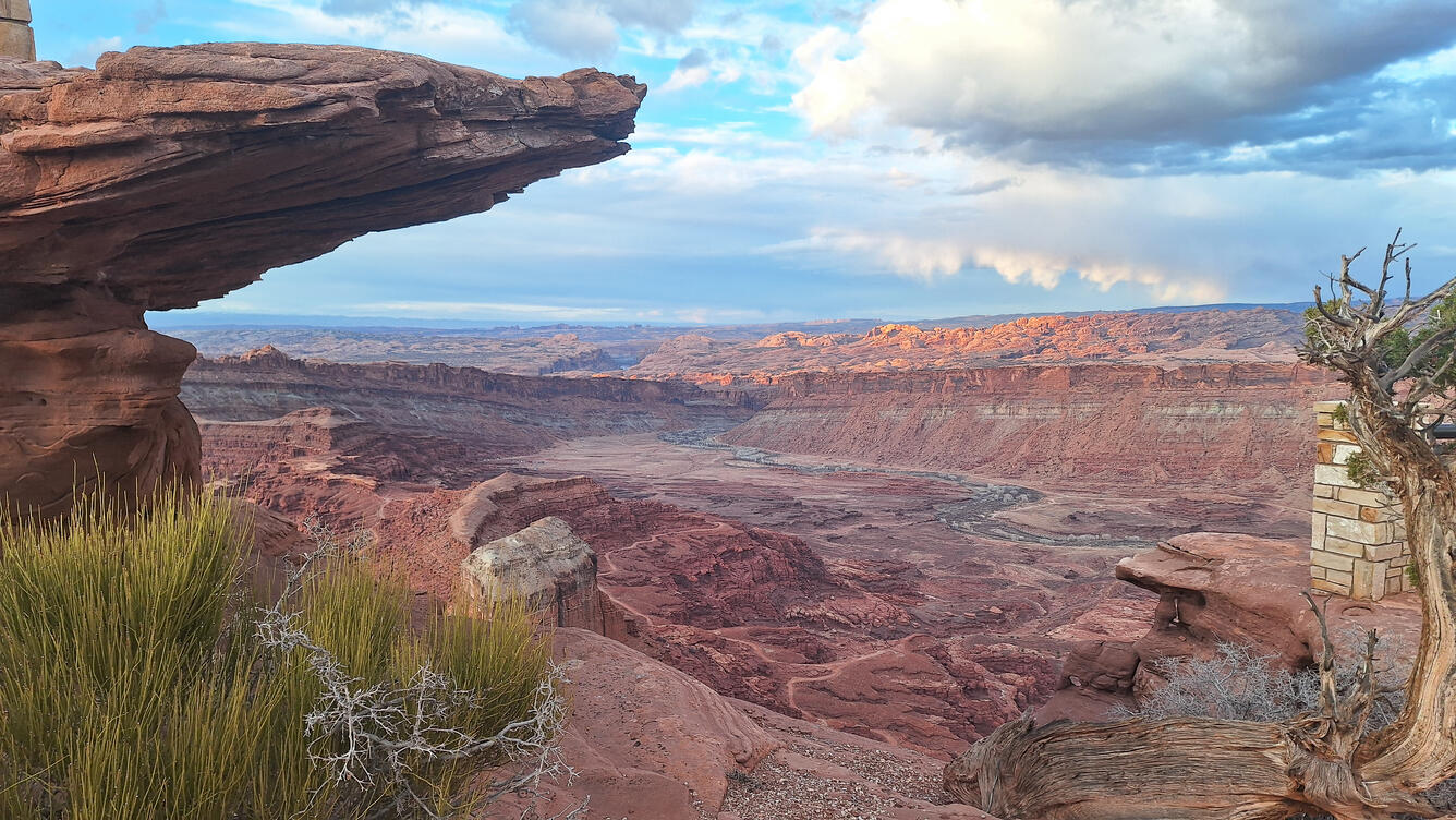 a reddish canyon with high rocks on either side, partly cloudy skies, cliff and grass in foreground