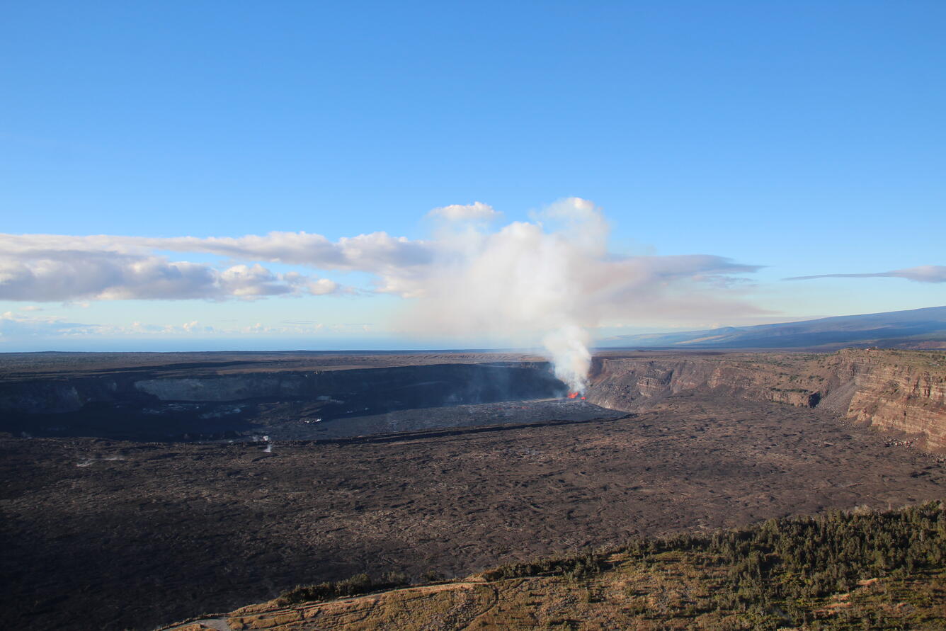Aerial overview of Kīlauea summit caldera and white gas plume rising from eruption in crater