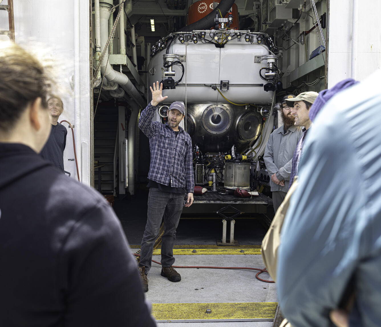 A person stands in front a white submersible while talking to a group of people