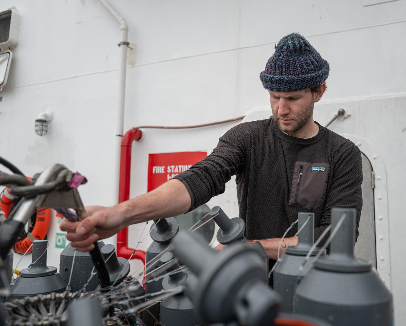 A person in a hat works on Niskin bottles attached to a CTD