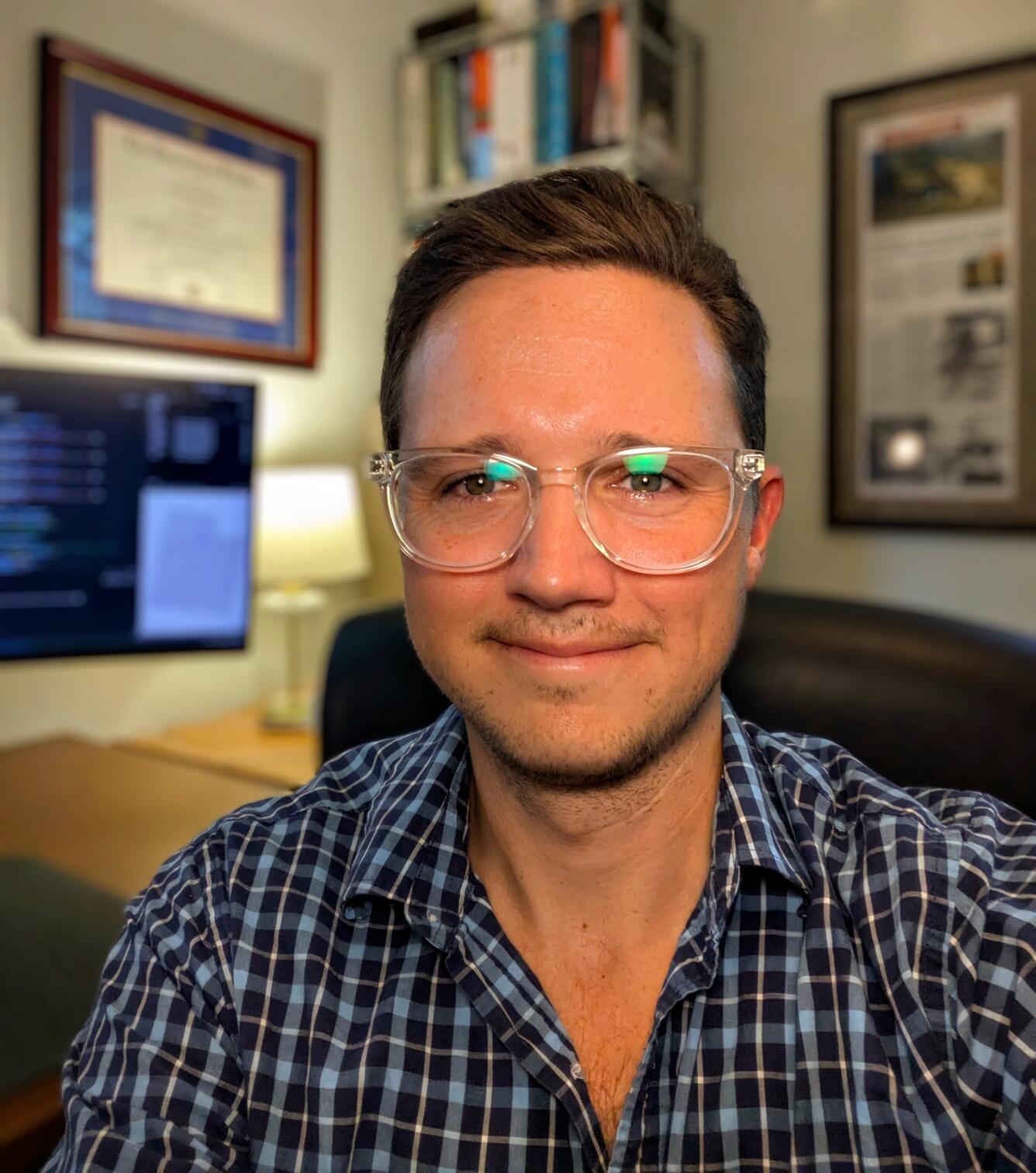 A man with short dark hair and glasses smiles for his picture.