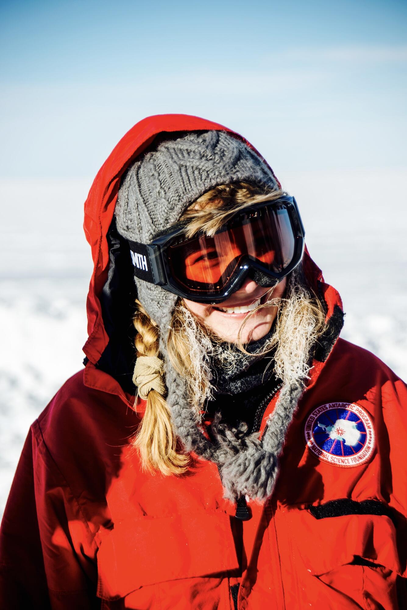 person with red coat, goggles and braids smiling