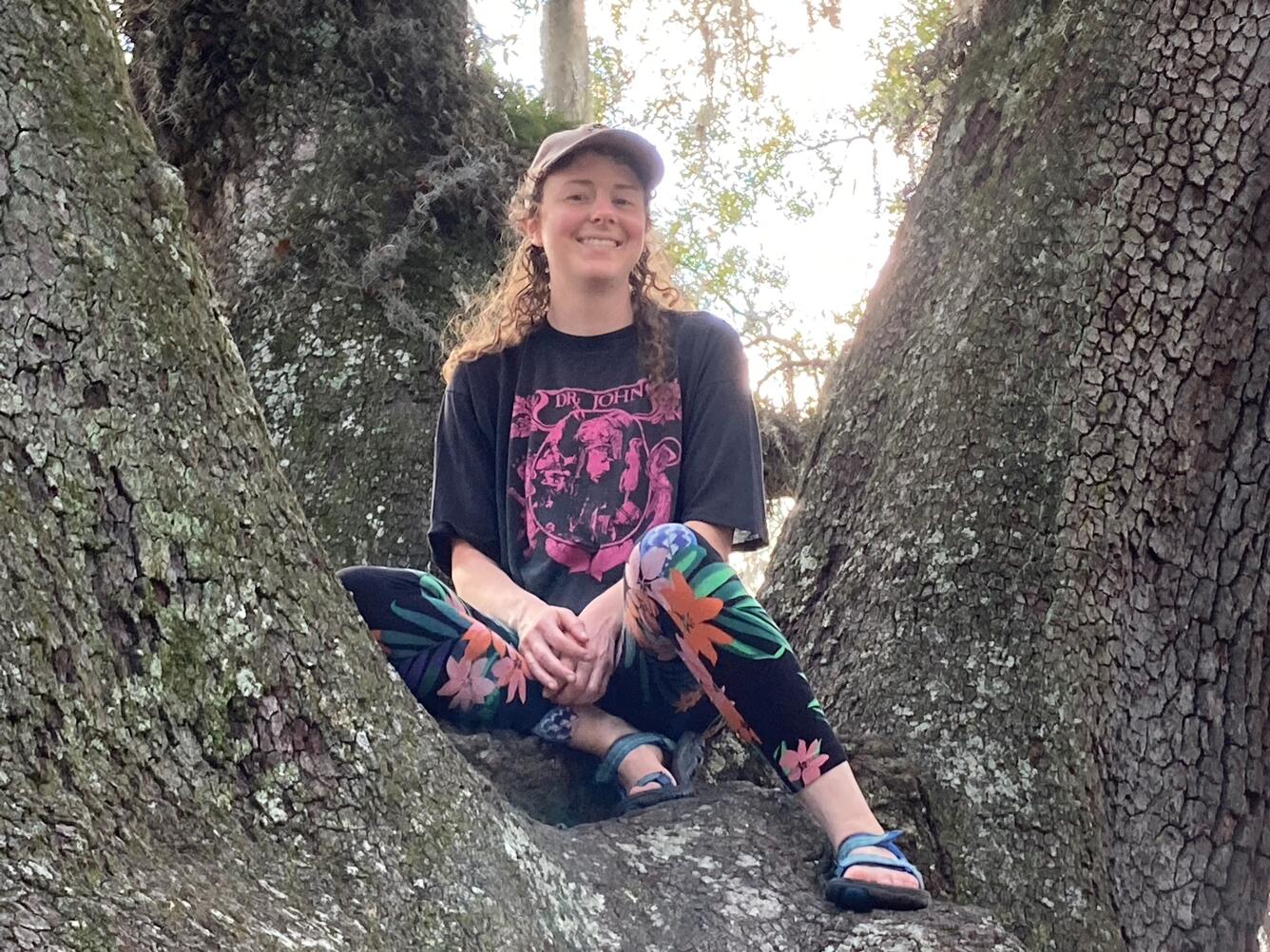 Ali Moss sits in within splayed tree trunks, smiling