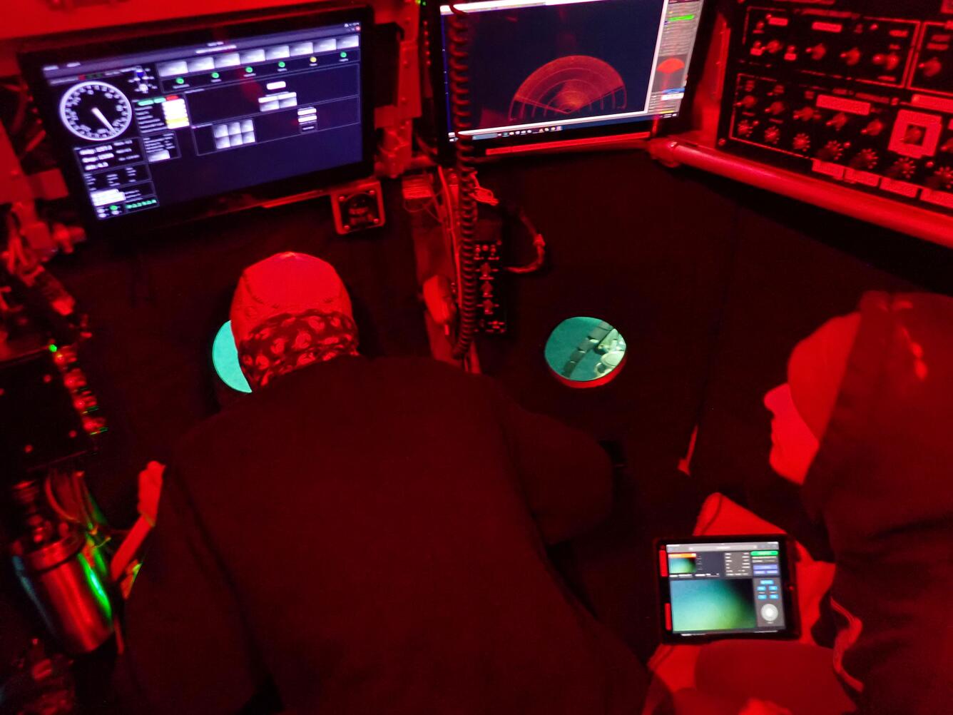 Red light glows over a pilot and the inside of the Alvin submersible