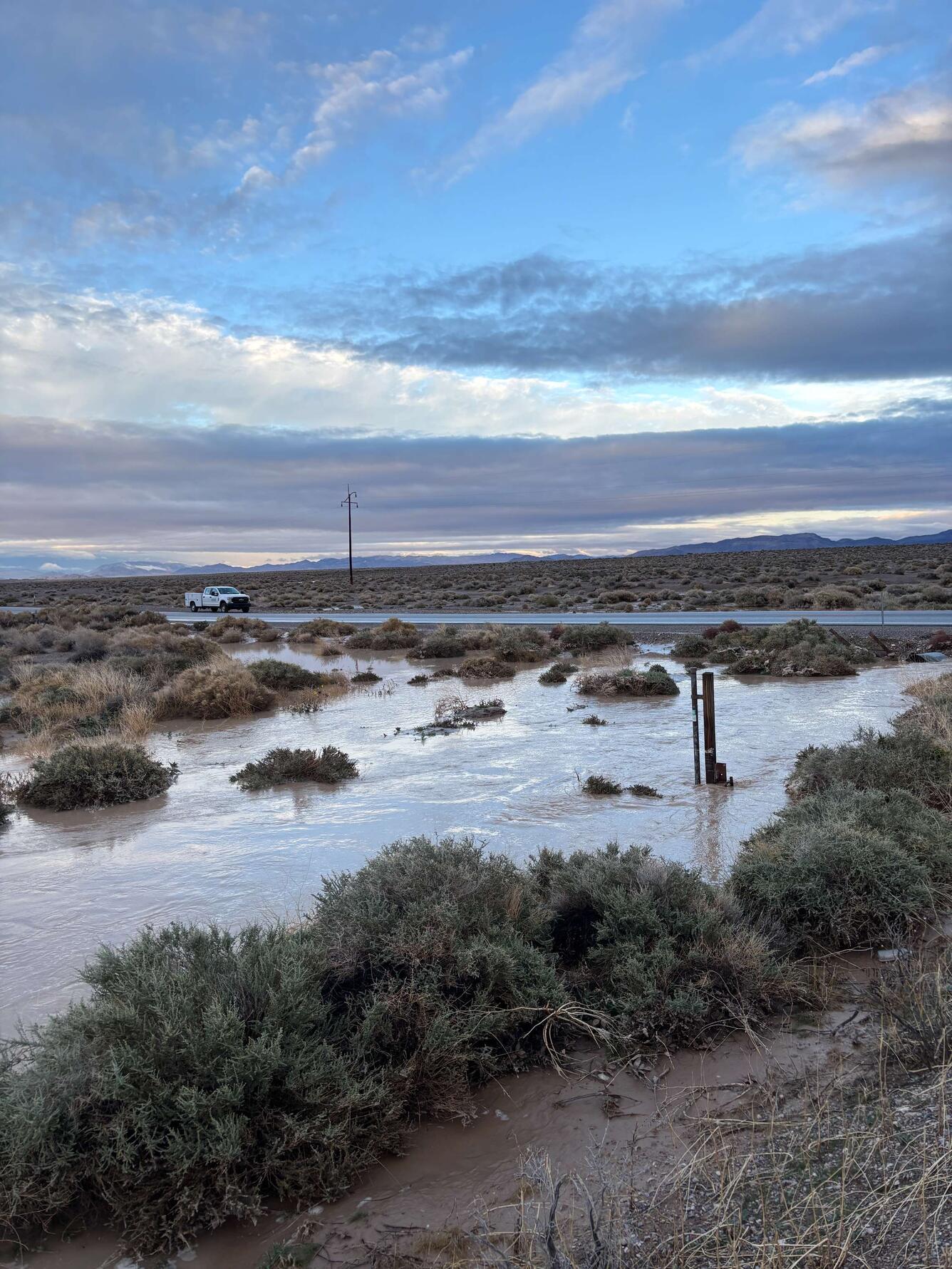 White USGS truck on road behind swollen Amargosa River at dusk with silhouetted mountains.