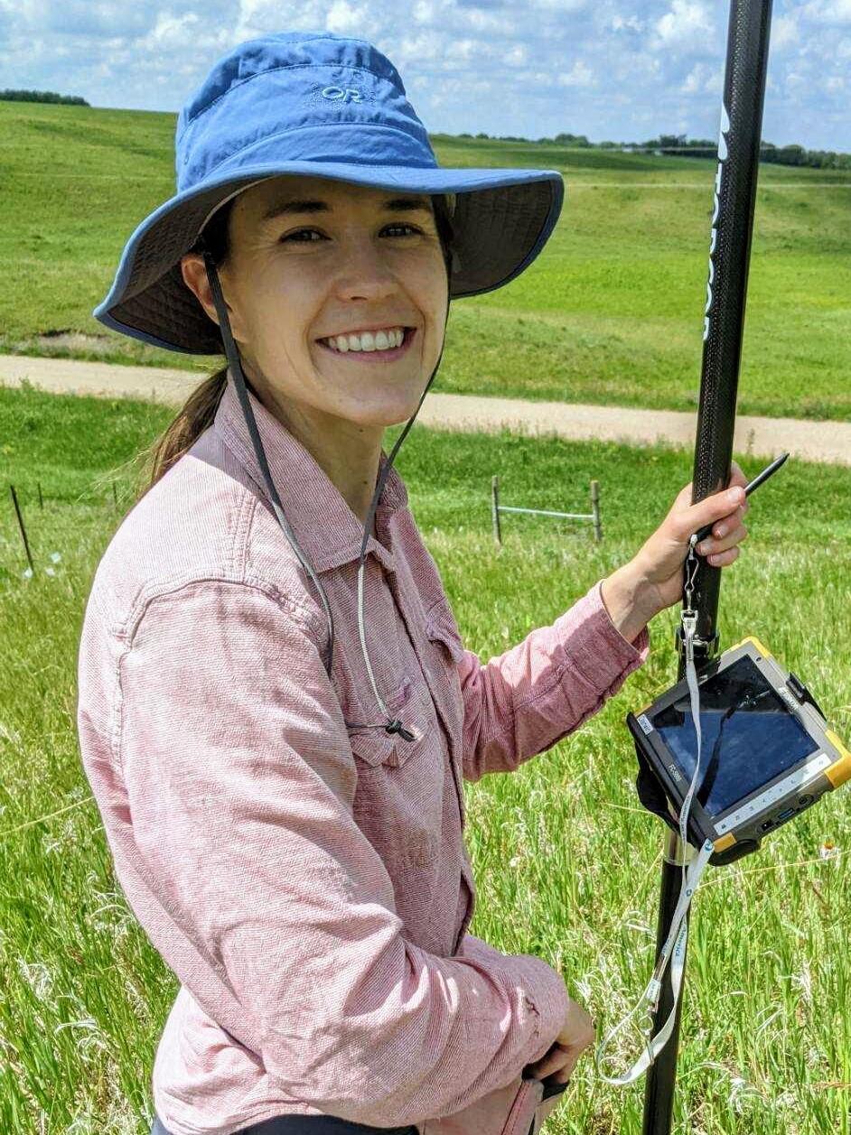 A woman in a blue hat and a light pink button up doing fieldwork.
