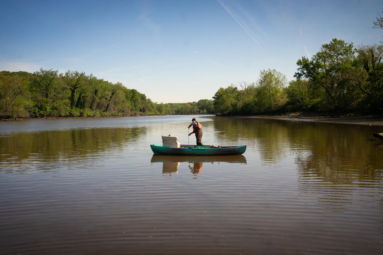 A hydrologic technician takes a water sample from a canoe.