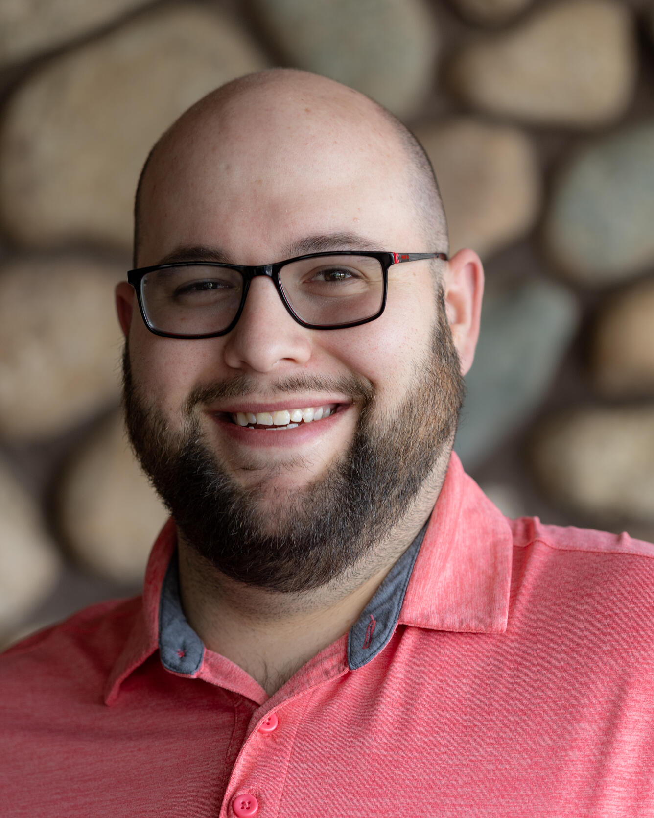 Smiling man with glasses standing in front of stone background